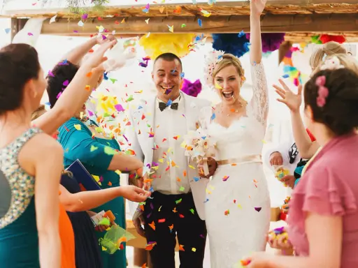 Glückliches Brautpaar im Konfettiregen, eine wunderschöne Tradition zur Hochzeit. Gäste werfen bunte Papierstreifen.