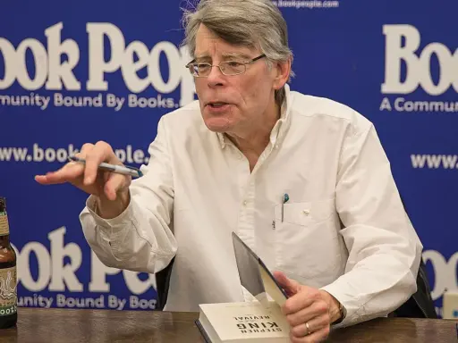 Stephen King, autore di libri da brivido, firma un volume. Sul tavolo, una bottiglia di root beer.