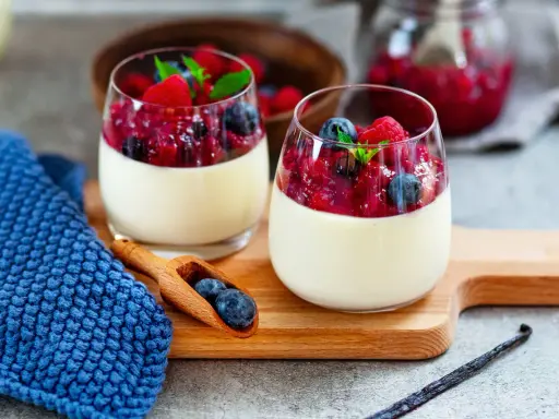Zwei Gläser mit cremigem Panna Cotta, garniert mit Beeren und Minze. Ein köstliches Rezept für original italienische Panna Cotta.