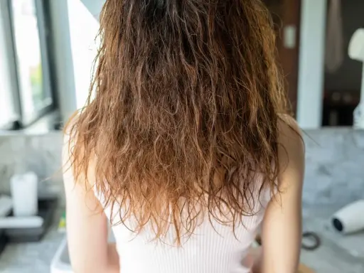Wilgotne, brązowe włosy z widocznym **frizz** opadają na ramiona.