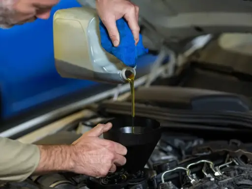 Mecánico vertiendo aceite nuevo en el motor para el mantenimiento del coche.