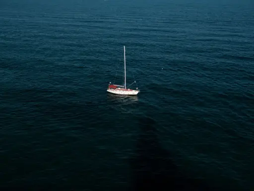 Un voilier blanc et rouge est au mouillage sur une mer sombre. La question est : combien de temps peut on rester au mouillage dans ce décor paisible ?