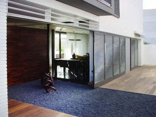 Una moderna casa con una contraventana corredera de lamas metálicas que protege un comedor interior.