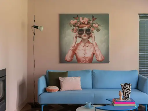 Ein hellblaues Sofa mit Kissen vor einem Bild, das eine Frau mit Blumenkranz und Schmetterlingen zeigt. Ein Beispiel für die Wohntrends 2026.