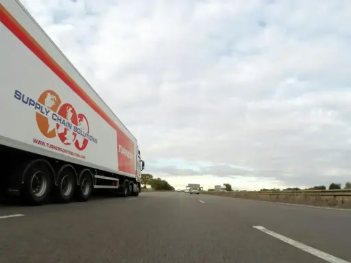 Camión de carga con el logo "Supply Chain Solutions" y "Turners" avanza por la autopista.