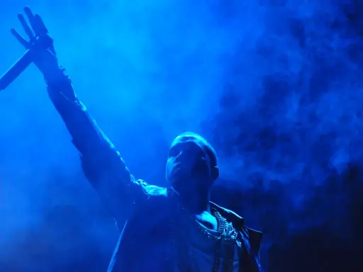 Kanye West z mikrofonem w dłoni, w niebieskiej poświacie. W tle dym, przypominający atmosferę z jego albumów.