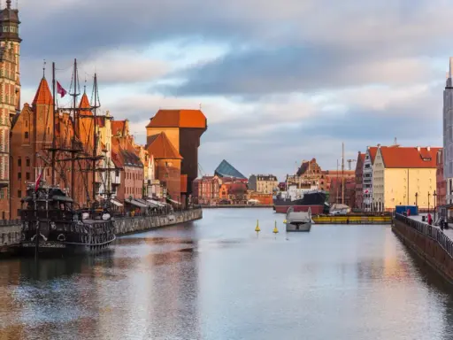 Gdańsk: zabytkowy żaglowiec cumuje przy Motławie, w tle Żuraw i nowoczesne budynki. Malowniczy opis miasta.