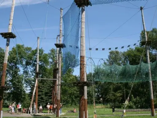 Śląski park linowy z drewnianymi słupami, siatkami i platformami na wysokości. Ludzie przygotowują się do zabawy.
