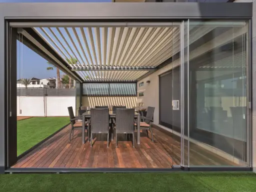 Porches cerrados con encanto, con mesa y sillas de mimbre sobre tarima de madera y césped artificial.