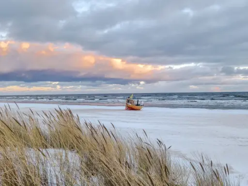 Ein kleines Boot liegt am verschneiten Strand der Ostsee, im Hintergrund die Seebrücke von Ahlbeck.