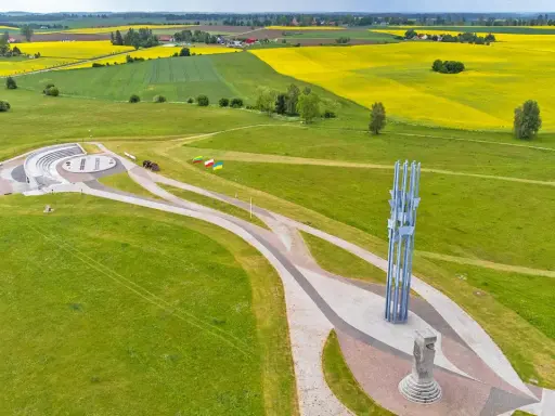 Pomnik i amfiteatr na polach grunwaldzkich, otoczone zielonymi łąkami i kwitnącymi polami rzepaku.