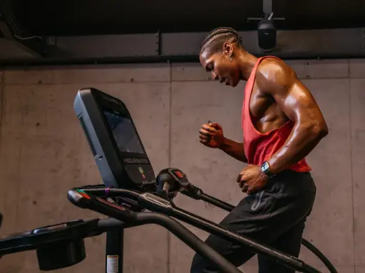 Schwitzender Mann im roten Tanktop läuft auf Laufband. Perfektes Cardio nach dem Krafttraining.