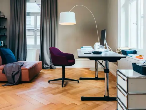 Accogliente stanza studio piccola con divano in pelle, scrivania regolabile, sedia viola e libreria a muro.