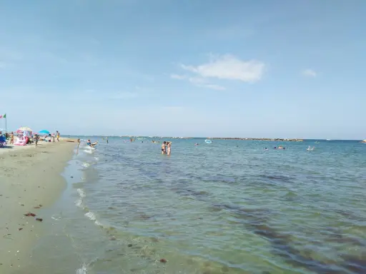 Gente che si gode il sole e il mare a Lido Adriano. Bambini giocano sulla sabbia, adulti nuotano e si rilassano nell'acqua cristallina.