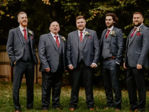 Five men in matching grey suits with red ties and pocket squares. The price of tuxedos can vary, but these look like a good investment for a wedding party.