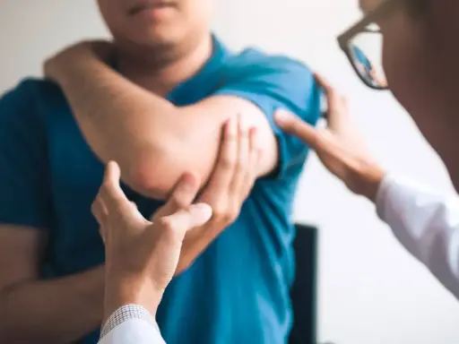Un médecin examine le coude d'un patient, possiblement atteint du syndrome de la souris, une maladie professionnelle liée à l'usage intensif de l'ordinateur.