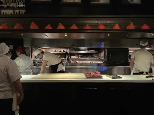 Chefs preparan cortes de carne en la parrilla Don Julio, con brasas ardientes y un ambiente de cocina profesional.
