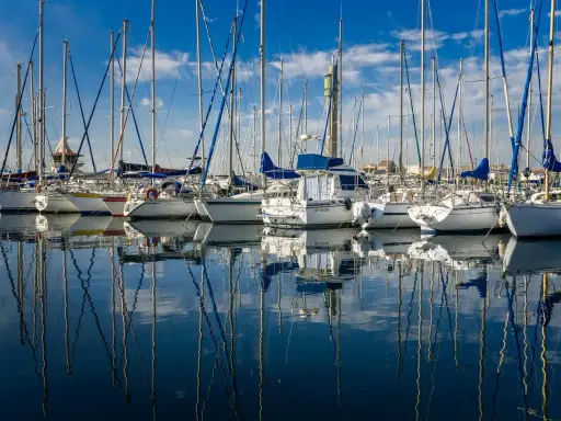 Une flotte de voiliers anglais, leurs mâts élancés se reflétant sur l'eau calme d'un port sous un ciel bleu éclatant.