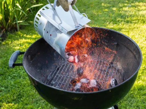 Encendiendo carbón con un chimenea para barbacoa. Chispas vuelan mientras se vierten las brasas calientes.