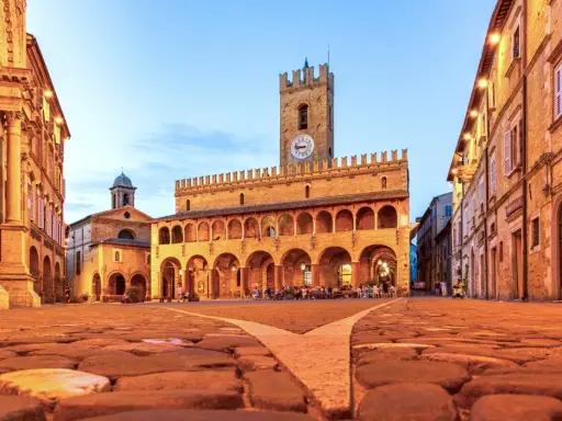 Piazza del Popolo a Ripatransone, un gioiello per un itinerario Marche 5 giorni. Edifici storici illuminati, torre con orologio e ciottoli antichi.