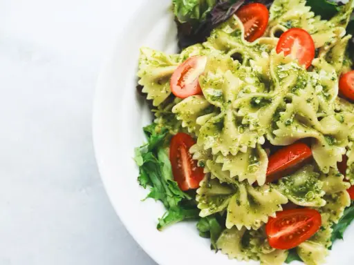 Pyszna sałatka z makaronem farfalle w sosie pesto, z pomidorkami koktajlowymi i świeżą sałatą.