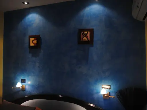 Pared azul con efecto veladura, dos cuadros abstractos y lámparas de pared.