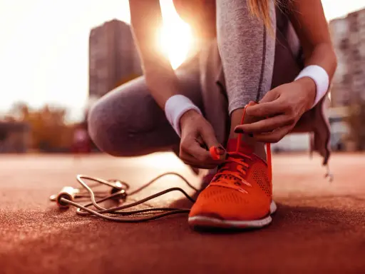 Frau bindet ihre neuen laufschuhe ein. Die Sonne scheint, ein Springseil liegt bereit.