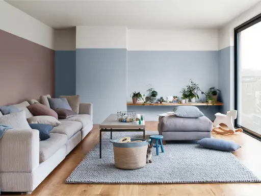 Soggiorno accogliente con divano beige, tappeto grigio e pareti color carta da zucchero. Un coniglietto curioso osserva dal cesto.