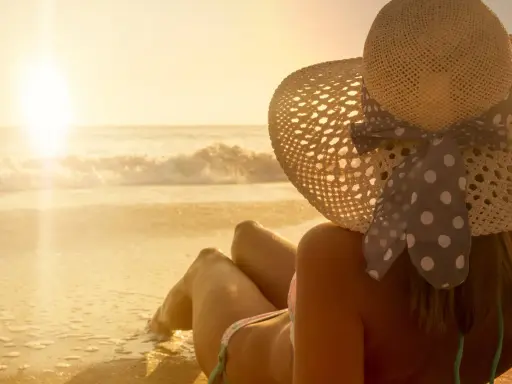 Donna con cappello di paglia e un bikini a pois, godendosi il tramonto sulla spiaggia. La sua pelle ha una perfetta abbronzatura arancione.