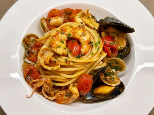 Spaghetti allo scoglio with shrimp, mussels, clams, squid, and cherry tomatoes in a white bowl.