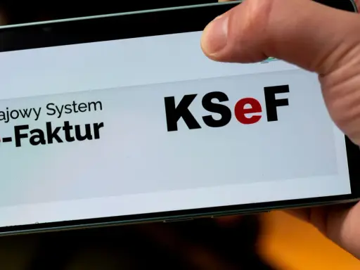 Palec dotyka ekranu telefonu z napisem "Krajowy System e-Faktur KSeF". To część polskiego ładu w finansach.
