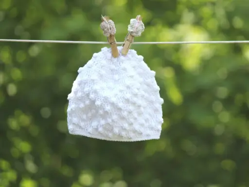 Vit virkad mössa med popcornmaskor hänger på en lina.