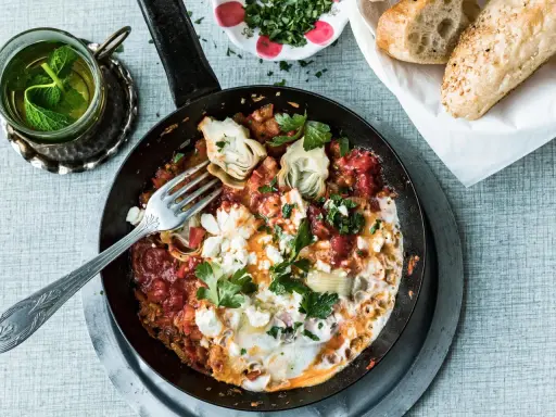 Herzhaftes Menemen ohne Ei mit Artischocken und Feta, garniert mit Petersilie. Dazu frisches Brot und Minztee.