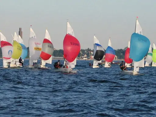 Bunte Segel dominieren das Bild einer spannenden Regatta. Mehrere kleine Boote mit Seglern sind auf dem Wasser unterwegs.