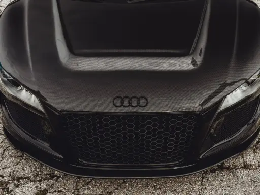 Przód czarnego Audi z maską z włókna węglowego. Widoczne reflektory, atrapa chłodnicy i logo marki.