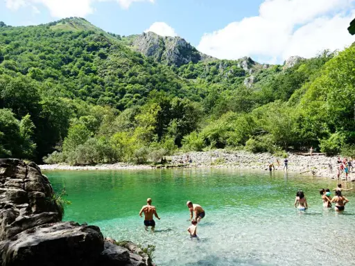 Gente disfrutando del agua cristalina en la olla de San Vicente, rodeada de exuberante vegetación y montañas.