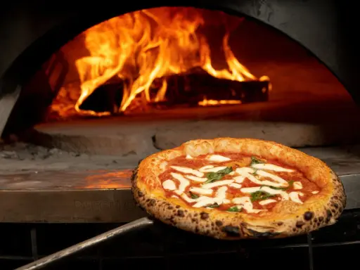 En perfekt italiensk pizza med mozzarella och basilika tas ur en vedeldad ugn med flammande eld.