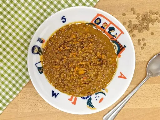 Un plato de lentejas bebé, cocinadas con zanahoria y especias, servido en un plato infantil con dibujos.