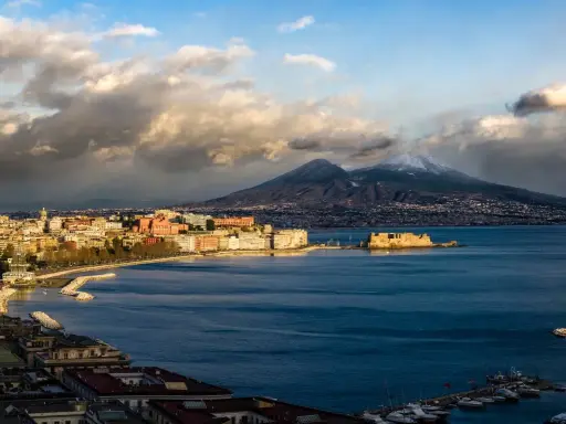 Vista panoramica di Napoli con il Vesuvio innevato sullo sfondo, il Castel dell'Ovo e il lungomare.