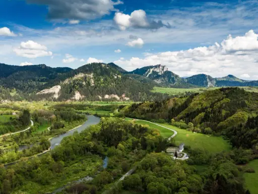 Malownicze **Pieniny** w okolicach **Szczawnicy** z meandrującym Dunajcem, zielonymi łąkami i skalistymi szczytami pod błękitnym niebem.