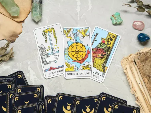 Karta życia tarot: As Mieczy, Koło Fortuny i Król Buław. Tajemnicze kryształy i stare księgi dopełniają mistyczną atmosferę.