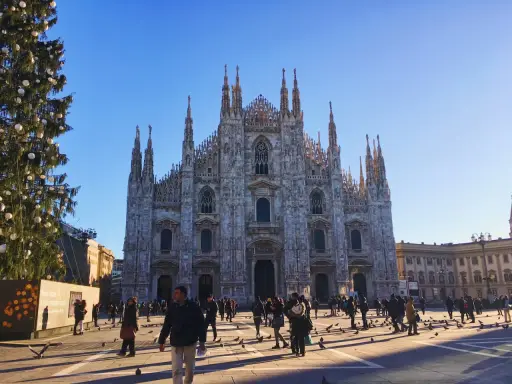 Le majestueux Duomo di Milano se dresse sous un ciel bleu, entouré de passants et d'un sapin de Noël décoré.