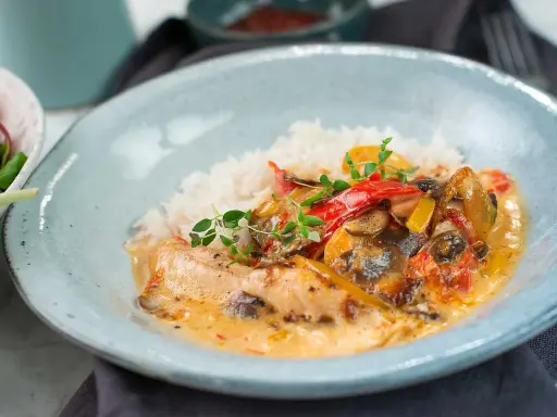 En krämig kyckling- och risrätt med paprika och svamp, garnerad med färska örter. En härlig måltid som ser utsökt ut.