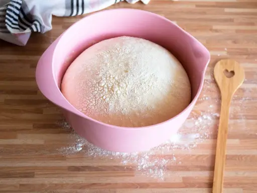 Ein aufgegangener Hefeteig in einer rosa Schüssel, bereit für neue Backideen. Daneben liegt ein Holzlöffel mit Herz.