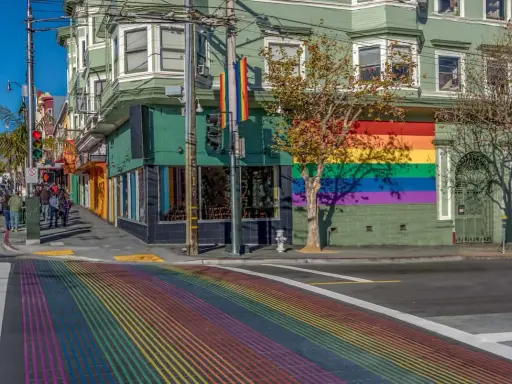 A vibrant rainbow crosswalk leads to a building adorned with a large rainbow mural, a symbol of the gay bed breakfast scene in San Francisco.