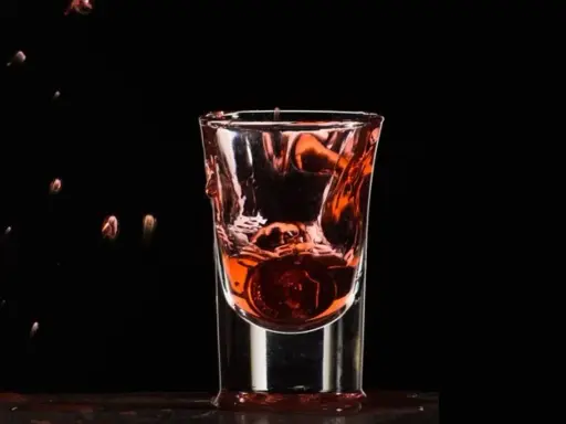 Wściekły pies drink, moneta spada do kieliszka z czerwonym płynem, tworząc fontannę.