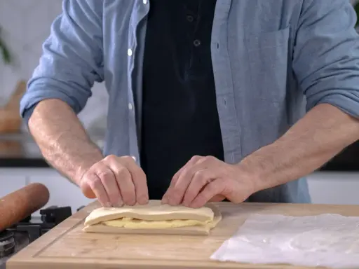 Un homme plie une pâte feuilletée professionnelle sur une planche en bois, prêt à créer des couches parfaites.