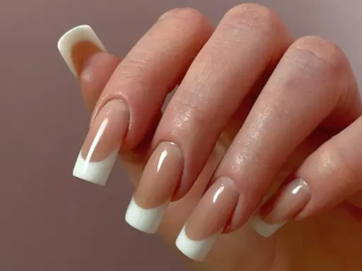 Dłoń z paznokciami w stylu odwrócony french. Klasyczny manicure z białym wykończeniem i naturalnym kolorem płytki.