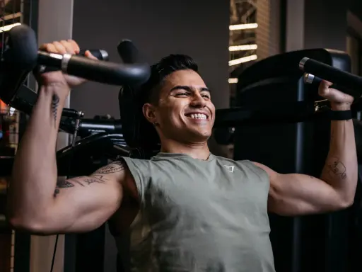 Ein Mann trainiert im Fitnessstudio, um seinen Brustmuskel aufzubauen. Er lächelt zufrieden, während er die Gewichte hebt.