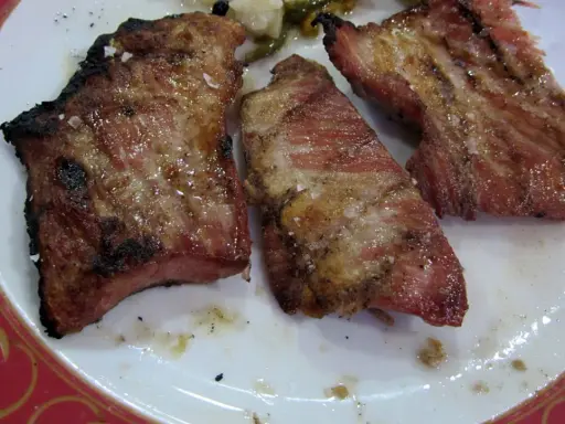 Tres trozos de lomo de cerdo al horno jugoso, con costra dorada y sal gruesa, servidos en un plato blanco con borde rojo.